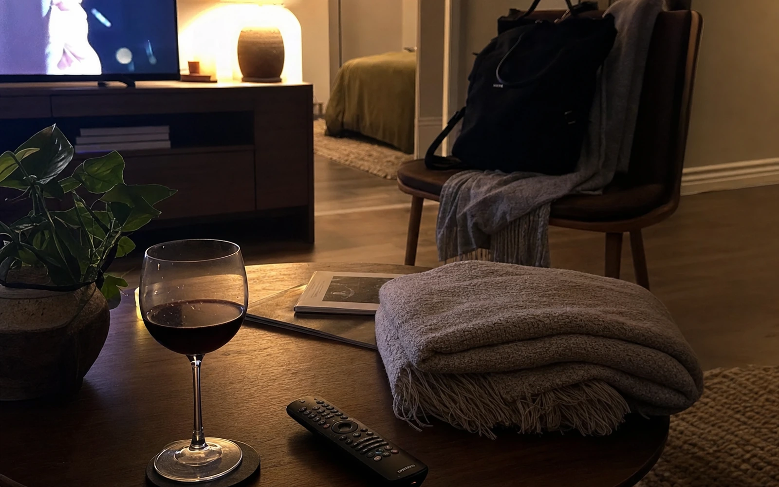 Weeknight living room with a wine glass, remote, folded blanket, and work bag.