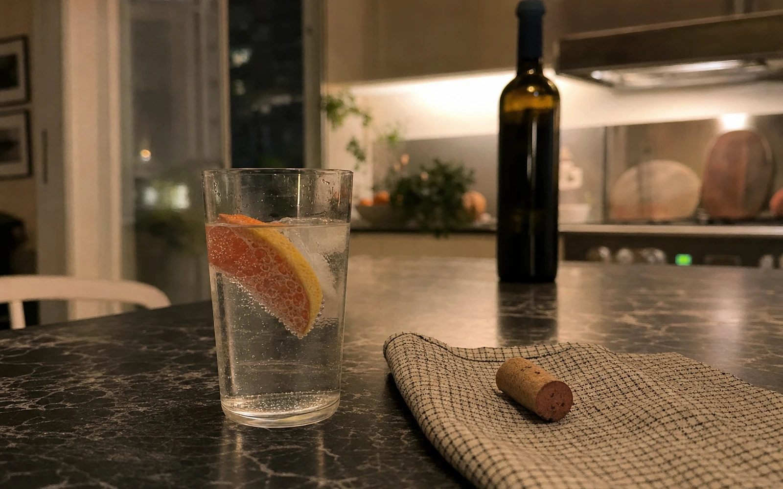 Evening kitchen counter with a sparkling water and grapefruit slice beside a corked bottle of wine.