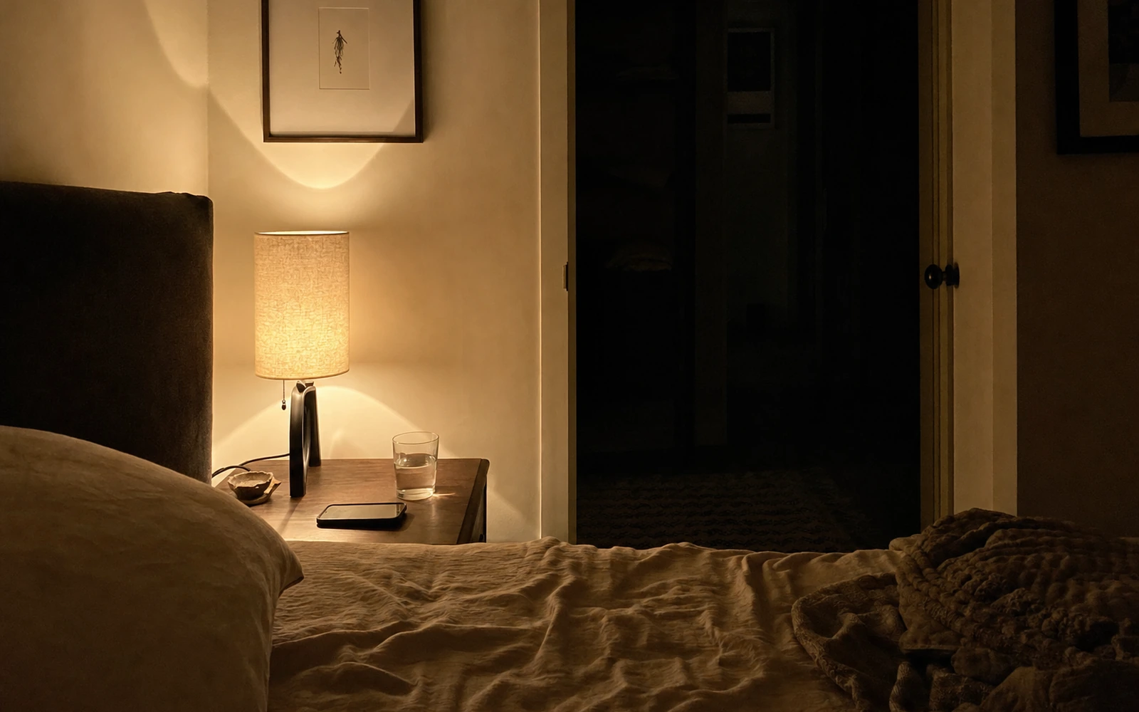 Quiet bedroom at night with a bedside lamp, phone, and water glass.